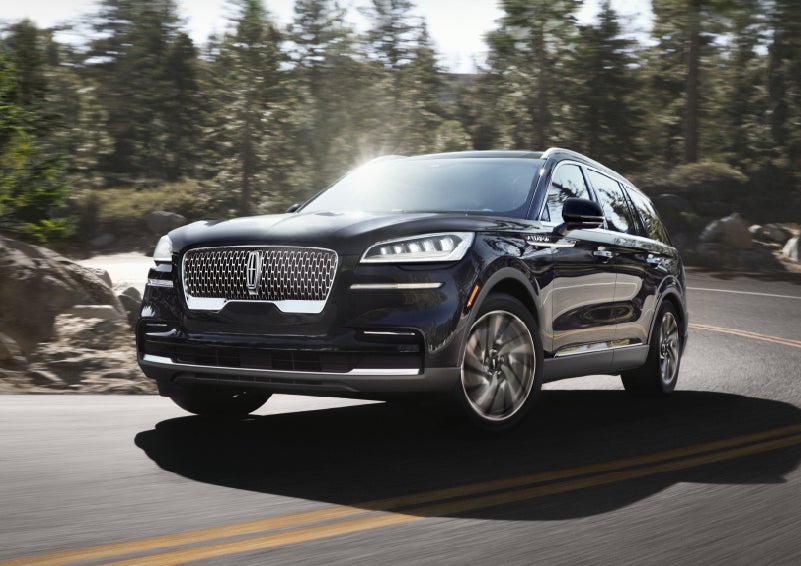 A Black Lincoln Aviator driving on a scenic road with trees and rocks in the background