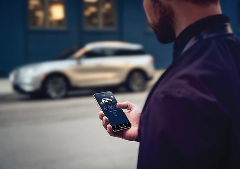 A person is shown interacting with a smartphone to connect to a Lincoln vehicle across the street. | Al Packer Lincoln in West Palm Beach FL
