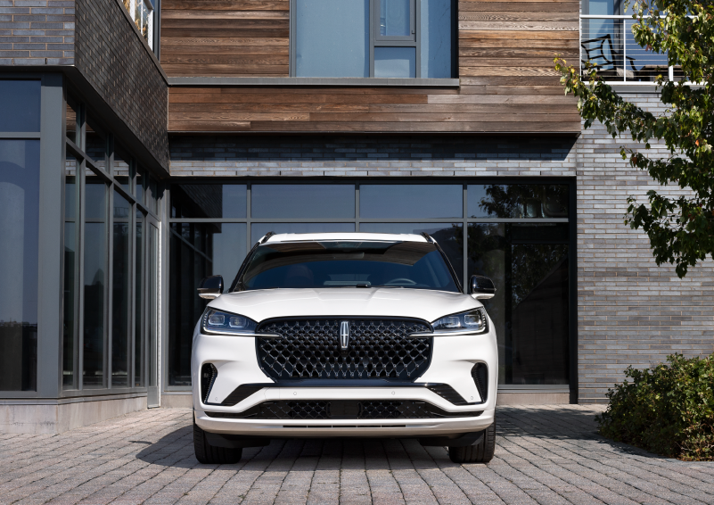 A white 2025 Lincoln Aviator® SUV is shown parked outside a modern building with gray brick and wood accents. | Al Packer Lincoln in West Palm Beach FL