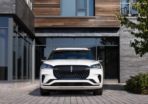 A white 2025 Lincoln Aviator® SUV is shown parked outside a modern building with gray brick and wood accents. | Al Packer Lincoln in West Palm Beach FL