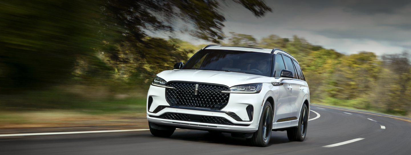 A white 2025 Lincoln Aviator® SUV is being driven down a road lined with trees. | Al Packer Lincoln in West Palm Beach FL