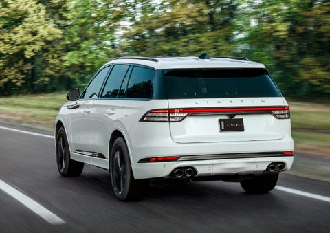 A white 2026 Lincoln Aviator® SUV is being driven away down a road lined with colorful trees. | Al Packer Lincoln in West Palm Beach FL
