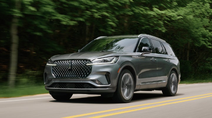 A 2027 Lincoln Aviator® SUV is being driven down a road lined with trees. | Al Packer Lincoln in West Palm Beach FL