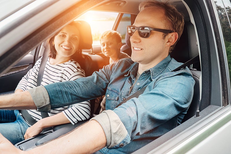 A family smiling while taking a trip in their car