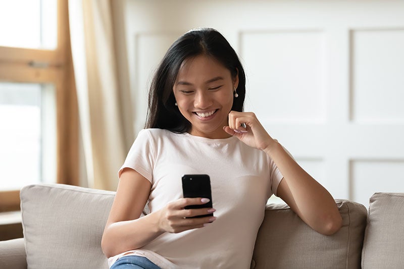 A woman sitting on a couch while looking and smiling at her phone
